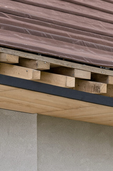Vue rapprochée d’un débord de toiture montrant le soffite, la planche de rive, les chevrons, la membrane d’étanchéité et la gouttière.