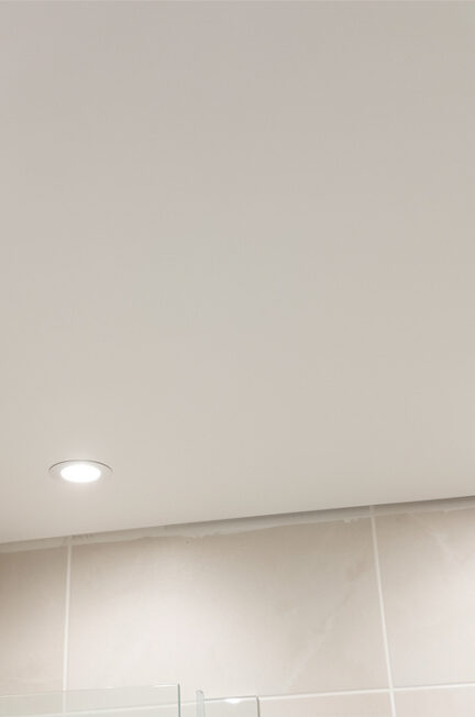 Plafond de salle de bain recouvert de lambris PVC blanc, équipé de spots encastrés et de joints soigneusement étanchéifiés.